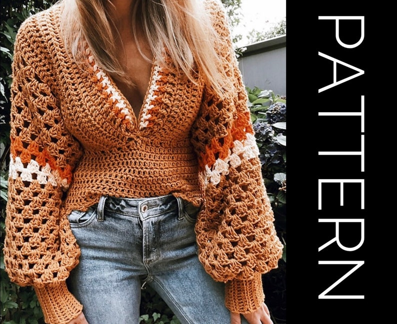 May include: A crocheted top with a V-neck and long sleeves. The top is made in a brown color with orange, white, and cream stripes. The top is worn over blue jeans.
