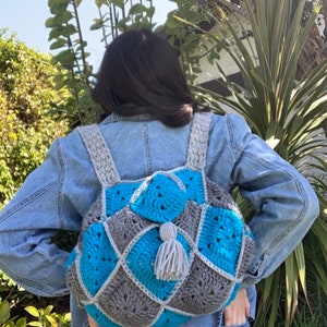 May include: A crocheted backpack with a grey and blue diamond pattern. The backpack has a grey tassel.