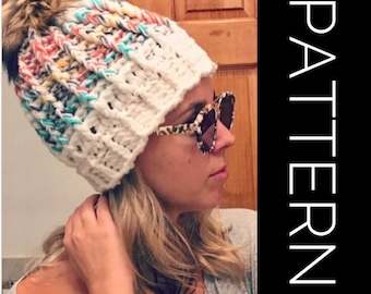 May include: A white crochet beanie with a colorful pom pom on top. The beanie has a white crocheted brim and a colorful crocheted top. The beanie is being worn by a person with blonde hair.
