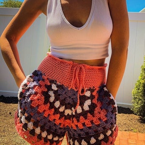 Puede incluir: Un par de pantalones cortos de crochet en tonos rosa, morado, blanco y marr&oacute;n. Los pantalones cortos tienen cintura alta y un lazo en la parte delantera.