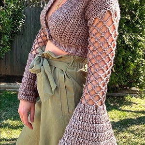 May include: A mauve crocheted crop top with bell sleeves and a lace-like pattern on the sleeves. The top is worn with a green high-waisted skirt.