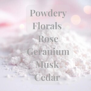 Może przedstawiać: Zbliżenie na stos białego proszku ze słowami "Powdery, Florals, Rose, Geranium, Musk, Cedar" na miękkim, rozmytym tle. Obraz sugeruje zapach lub produkt kosmetyczny o nutach kwiatowych i drzewnych.
