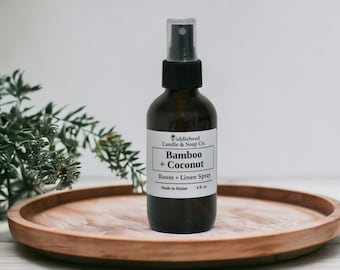 May include: A brown glass bottle with a black spray top and a white label. The label reads "iddlehead Candle & Soap Co. Bamboo + Coconut Room Linen Spray Made in Maine 4 fl. oz."