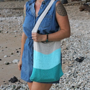 May include: A woman wearing a denim dress and a knitted tote bag with a striped pattern in shades of beige, light blue, and teal.