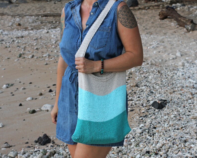 May include: A woman wearing a denim dress and a knitted tote bag with a striped pattern in shades of beige, light blue, and teal.