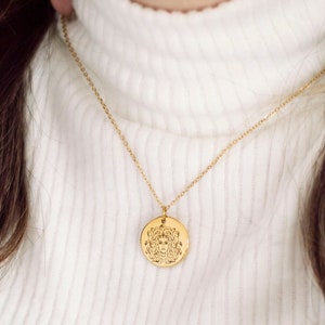 Woman wearing gold Medusa pendant necklace with white high neck top