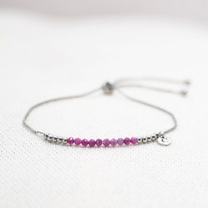 May include: A silver adjustable bracelet with a row of pink gemstone beads and a silver charm with a letter 'C'.