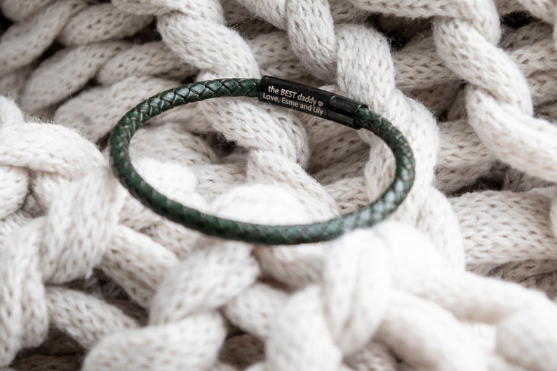 May include: A dark green leather bracelet with a black metal plate engraved with the text "the BEST daddy Love, Esme and Lily".