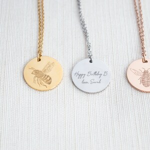 May include: Three gold, silver, and rose gold necklaces with round pendants featuring an engraved bee design. The silver pendant has the text "Happy Birthday B love, Sarah" engraved on it.