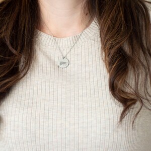 May include: A woman wearing a light beige ribbed sweater with a silver chain necklace and a round pendant.