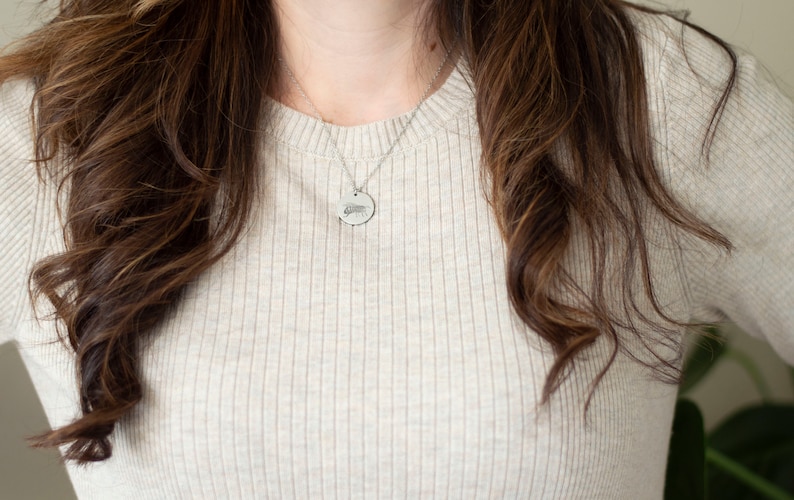 May include: A woman wearing a light beige ribbed sweater with a silver chain necklace and a round pendant.