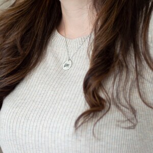 May include: A woman wearing a light beige ribbed sweater with a silver chain necklace and a small oval pendant.