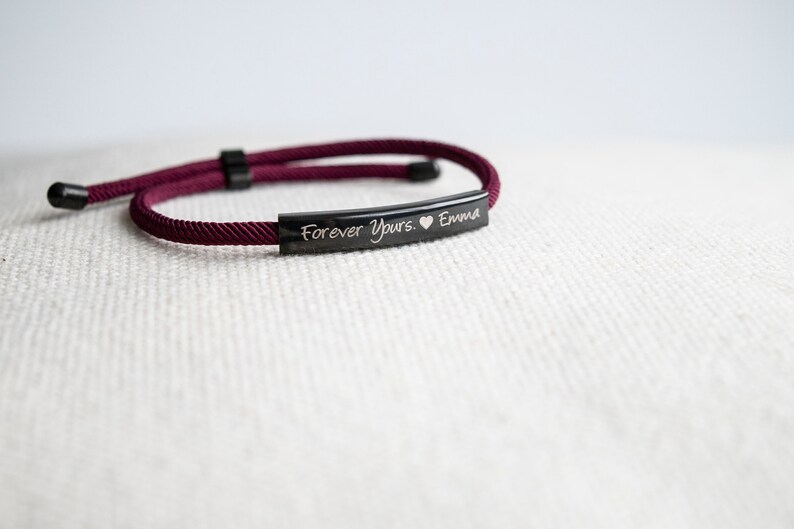 Op de afbeelding: Burgundy rood gevlochten koord armband met een zwarte metalen balk gegraveerd met de tekst "Forever Yours. &hearts; Emma"