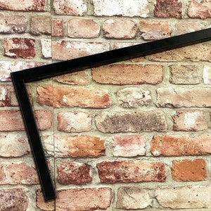 May include: Black metal shelf bracket with a 90-degree angle. The bracket is mounted on a brick wall.