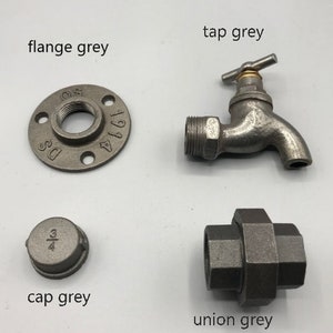 May include: A set of four grey metal plumbing fittings, including a flange, a cap, a union, and a tap. The flange is marked with the numbers "1 1/4" and "DS". The cap is marked with the fraction "3/4".