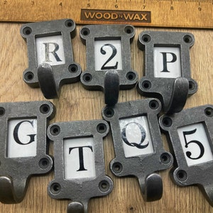 May include: Set of eight metal hooks with a black finish. Each hook has a rectangular frame with a white background and a black letter or number in the centre. The letters are R, 2, P, G, T, Q, and 5.