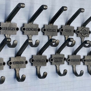 May include: Set of 10 double hooks with a rectangular metal plate featuring the names of different cities and regions in the United Kingdom. The hooks are silver in colour and have a rustic finish.