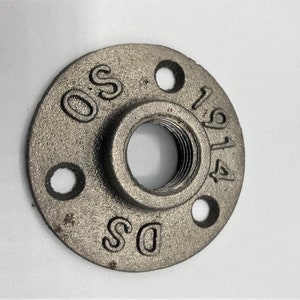 May include: A silver metal pipe fitting with a threaded hole in the centre and three smaller holes around the edge. The fitting is marked with the letters "DS" and "OS" and the numbers "1914".