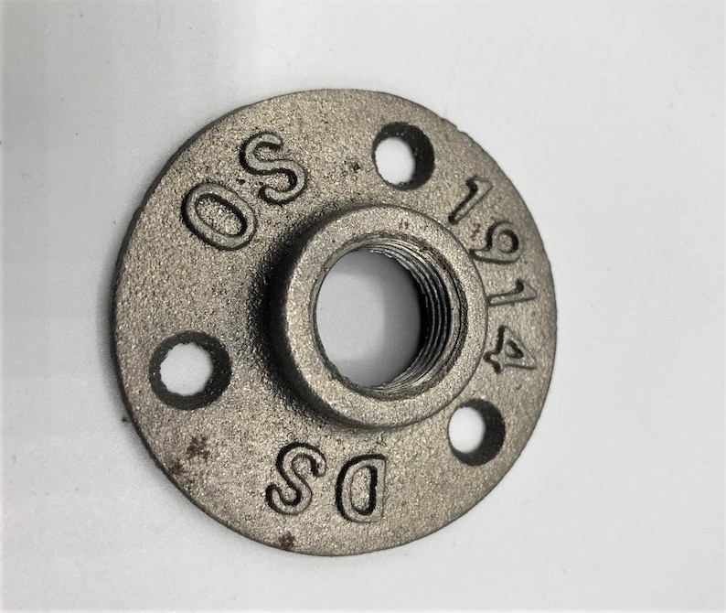 May include: A silver metal pipe fitting with a threaded hole in the centre and three smaller holes around the edge. The fitting is marked with the letters "DS" and "OS" and the numbers "1914".