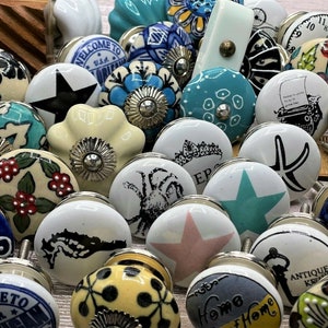 May include: Assortment of ceramic drawer knobs with various designs and colours. Some knobs feature floral patterns, others have nautical themes, and some have words like "Welcome to" and "Home".