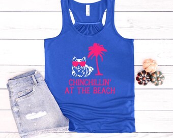 May include: A royal blue tank top with a white graphic of a chinchilla wearing sunglasses and a palm tree. The text "Chinchillin' at the Beach" is printed in pink below the graphic.