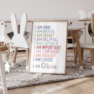 May include: A framed print with the text "I am kind, I am brave, I am smart, I am helpful, I am capable, I am important, I am confident, I am enough, I am loved, I am Olivia" in colorful text on a white background.