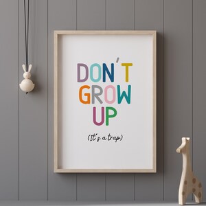 May include: A framed print with the text "DON'T GROW UP (It's a trap)" in colorful letters. The letters are in different colors, including pink, orange, green, blue, and yellow. The print is hanging on a gray wall.