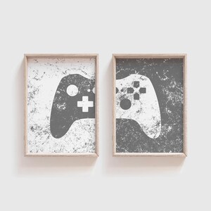 May include: Two framed prints with a distressed white background and a distressed gray background. Each print features a white silhouette of a video game controller.