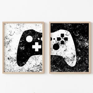 Peut inclure: Deux impressions encadrées en noir et blanc d'une manette de jeu vidéo. L'impression de gauche présente une manette noire sur fond blanc. L'impression de droite présente une manette blanche sur fond noir.