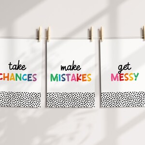May include: Three white prints with black polka dot borders hang on a white wall. The prints feature the words "take chances", "make mistakes", and "get messy" in colorful, handwritten lettering.