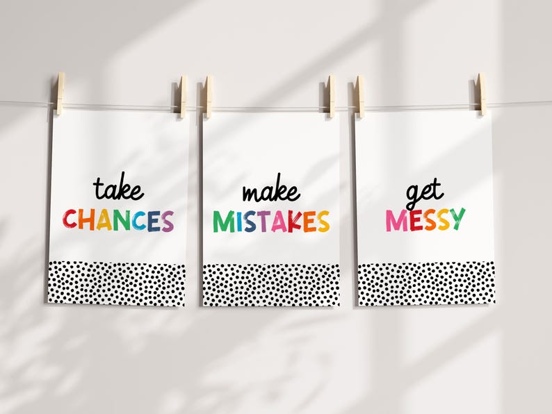 May include: Three white prints with black polka dot borders hang on a white wall. The prints feature the words "take chances", "make mistakes", and "get messy" in colorful, handwritten lettering.