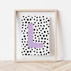 May include: A framed print with a white background and black polka dots. The letter "L" is in the centre of the print in a light purple colour.