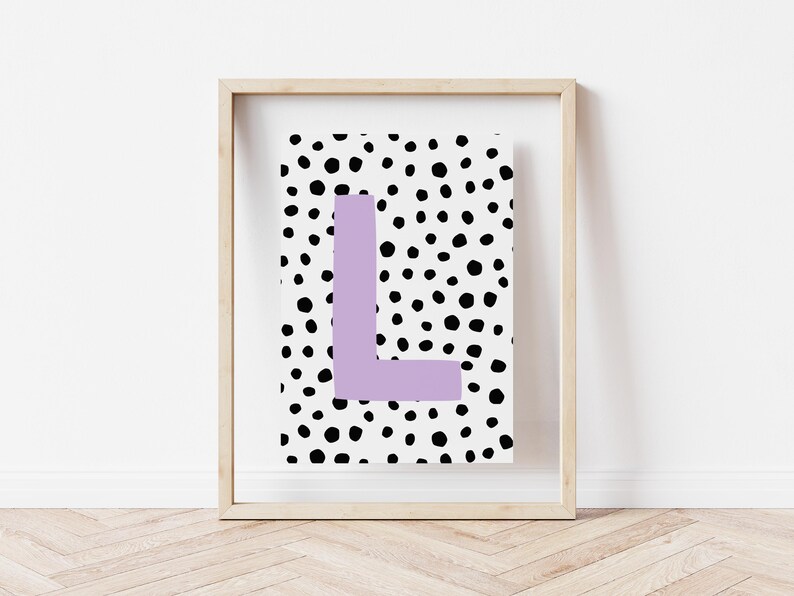 May include: A framed print with a white background and black polka dots. The letter "L" is in the centre of the print in a light purple colour.