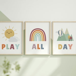 Puede incluir: Tres impresiones enmarcadas con ilustraciones y texto coloridos. La primera impresi&oacute;n presenta un sol amarillo con una cara sonriente y una nube blanca, con la palabra "PLAY" en colores arco&iacute;ris debajo. La segunda impresi&oacute;n presenta un arco&iacute;ris con rayas rojas, naranjas, amarillas, verdes, azules, &iacute;ndigo y violetas, con la palabra "ALL" en colores arco&iacute;ris debajo. La tercera impresi&oacute;n presenta una cordillera verde con un globo aerost&aacute;tico flotando arriba, con la palabra "DAY" en colores arco&iacute;ris debajo.