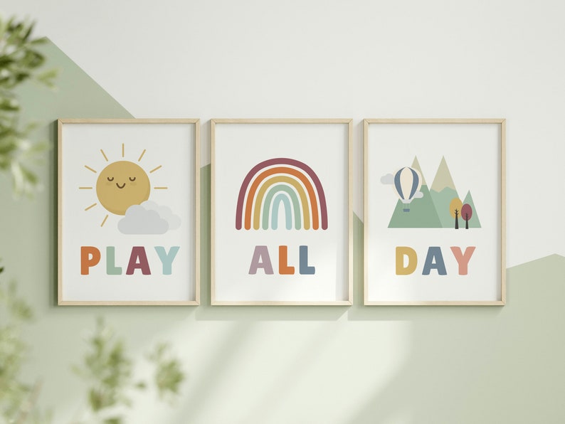 Puede incluir: Tres impresiones enmarcadas con ilustraciones y texto coloridos. La primera impresi&oacute;n presenta un sol amarillo con una cara sonriente y una nube blanca, con la palabra "PLAY" en colores arco&iacute;ris debajo. La segunda impresi&oacute;n presenta un arco&iacute;ris con rayas rojas, naranjas, amarillas, verdes, azules, &iacute;ndigo y violetas, con la palabra "ALL" en colores arco&iacute;ris debajo. La tercera impresi&oacute;n presenta una cordillera verde con un globo aerost&aacute;tico flotando arriba, con la palabra "DAY" en colores arco&iacute;ris debajo.