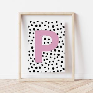May include: A framed print featuring a black and white polka dot pattern with a large pink letter "P" in the centre.