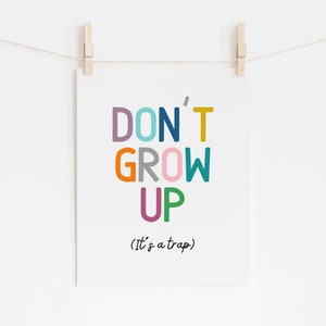 May include: A colorful print with the text "DON'T GROW UP (It's a trap)" in a playful font. The words are in different colors, including purple, blue, teal, yellow, orange, gray, pink, and green.