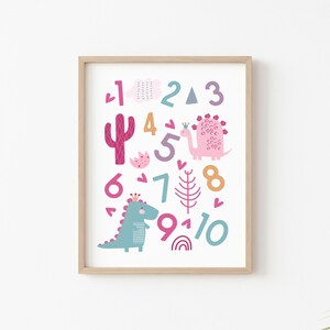 Puede incluir: Un p&oacute;ster imprimible colorido con dinosaurios rosas y azules, un cactus y los n&uacute;meros del 1 al 10. Los n&uacute;meros est&aacute;n en una variedad de colores y fuentes.