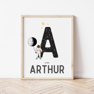 May include: A black and white letter A with stars and a moon. An astronaut is holding the moon. The text "A is for ARTHUR" is below the letter.