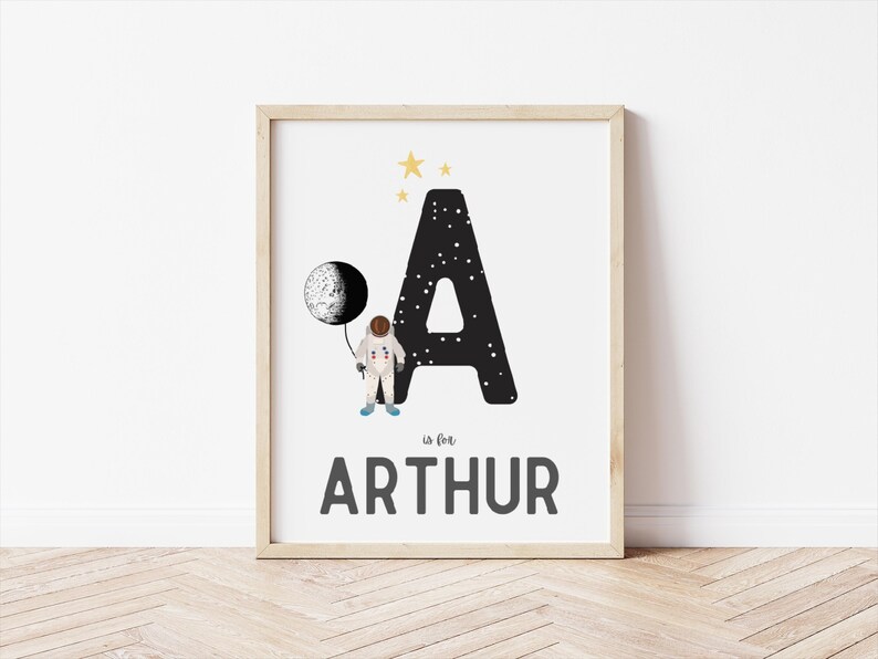 May include: A black and white letter A with stars and a moon. An astronaut is holding the moon. The text "A is for ARTHUR" is below the letter.
