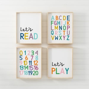 Puede incluir: Cuatro impresiones enmarcadas con texto colorido sobre un fondo de madera blanca. Las impresiones dicen "Let's Read", "ABCDE FGHIJK LMNOP QRSTU VWXYZ", "01234 5678 9 10 11 12 13141516 17181920", y "Let's Play".