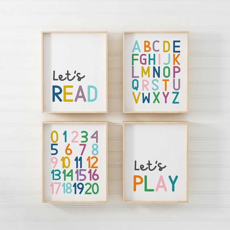 Puede incluir: Cuatro impresiones enmarcadas con texto colorido sobre un fondo de madera blanca. Las impresiones dicen "Let's Read", "ABCDE FGHIJK LMNOP QRSTU VWXYZ", "01234 5678 9 10 11 12 13141516 17181920", y "Let's Play".