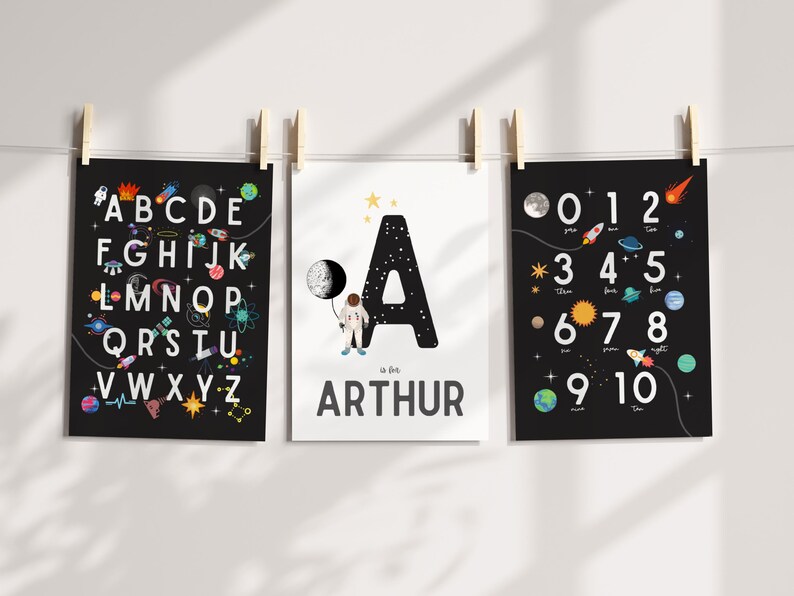 May include: Three black and white posters with a space theme. The first poster features the alphabet with space-themed illustrations. The second poster features the letter A with a spaceman holding a moon. The third poster features the numbers 0-10 with space-themed illustrations. The second poster also includes the name "Arthur".