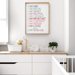 May include: A framed print with a white background and colorful text that reads "I am kind, I am brave, I am smart, I am helpful, I am capable, I am important, I am confident, I am enough, I am loved, I am Olivia".