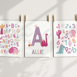 Puede incluir: Tres impresiones de arte de pared imprimibles con un tema de dinosaurio rosa y morado. La primera impresi&oacute;n muestra el alfabeto con un dinosaurio rosa. La segunda impresi&oacute;n muestra la letra A con un dinosaurio rosa y el nombre Allie. La tercera impresi&oacute;n muestra los n&uacute;meros del 1 al 10 con un dinosaurio rosa y un dinosaurio azul.