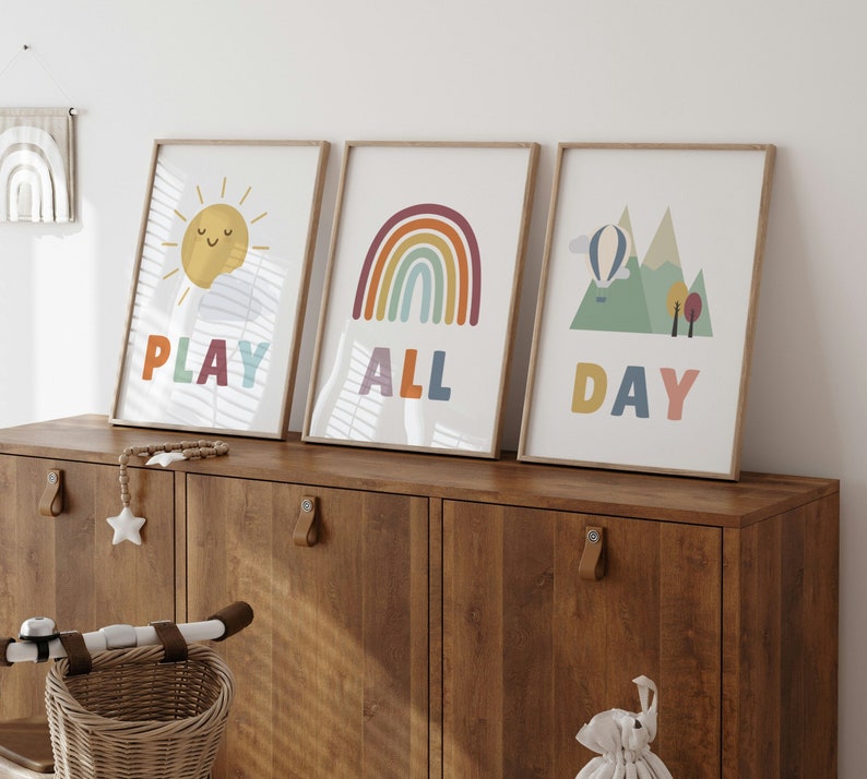 Puede incluir: Tres impresiones enmarcadas con ilustraciones y texto coloridos. La primera impresi&oacute;n presenta un sol amarillo con una cara sonriente y el texto "PLAY". La segunda impresi&oacute;n presenta un arco&iacute;ris con el texto "ALL". La tercera impresi&oacute;n presenta un globo aerost&aacute;tico y monta&ntilde;as con el texto "DAY".