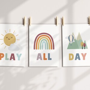 Puede incluir: Tres impresiones coloridas con ilustraciones de un sol, un arco&iacute;ris y monta&ntilde;as con un globo aerost&aacute;tico. El texto en las impresiones dice "PLAY ALL DAY".