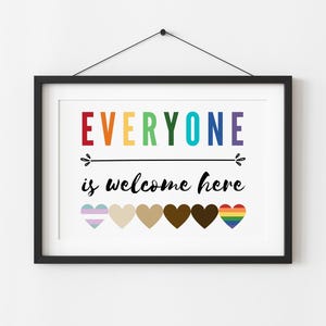 May include: A framed print with the text "EVERYONE is welcome here" in rainbow colors. The print features a row of seven hearts in different colors and patterns, including a rainbow heart, a transgender pride heart, and a brown heart.