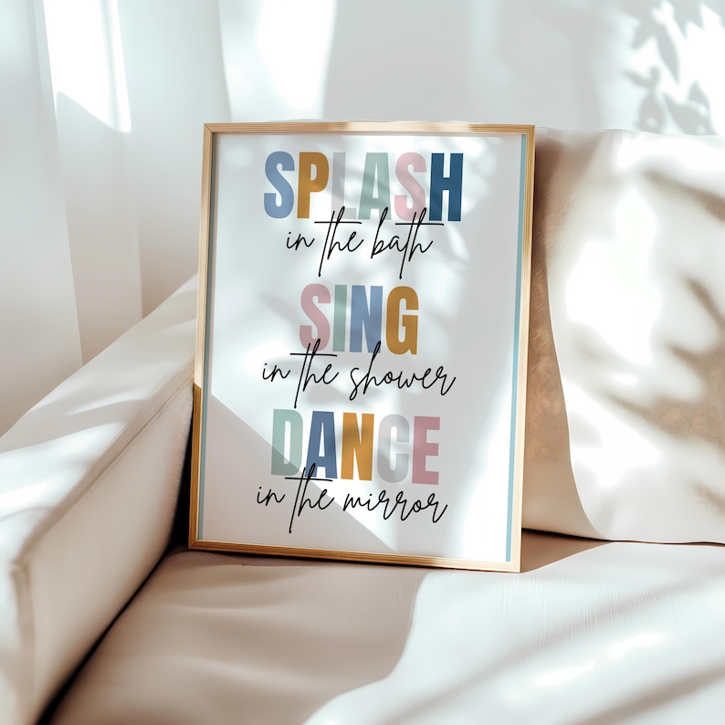 以下が含まれることがあります： カラフルな文字で「SPLASH in the bath SING in the shower DANCE in the mirror」と書かれた額装されたプリント。プリントは白い背景で、金色の額縁が付いています。