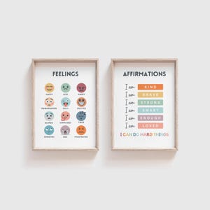May include: Two framed prints with colorful illustrations. The left print has the word "Feelings" at the top and shows 12 different emotions with corresponding emojis. The right print has the word "Affirmations" at the top and lists positive affirmations with the phrase "I am" repeated before each affirmation. The last affirmation reads "I can do hard things."